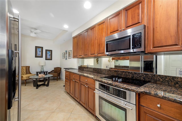 kitchen with light tile patterned floors, appliances with stainless steel finishes, dark stone counters, and ceiling fan