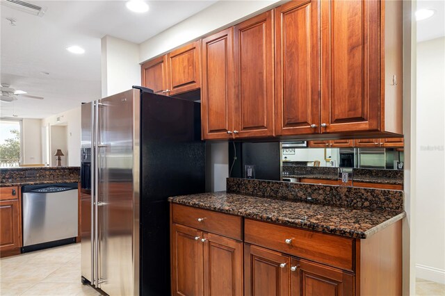 kitchen with appliances with stainless steel finishes, light tile patterned floors, dark stone counters, and ceiling fan