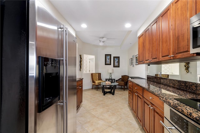 kitchen featuring ceiling fan, stainless steel appliances, light tile patterned floors, and dark stone countertops