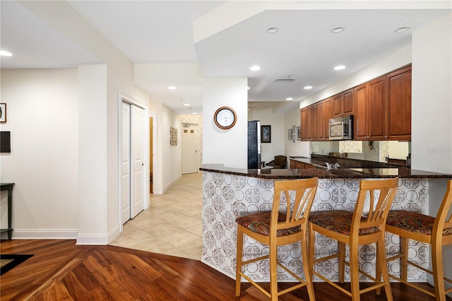 kitchen featuring a kitchen breakfast bar, kitchen peninsula, light wood-type flooring, and dark stone counters