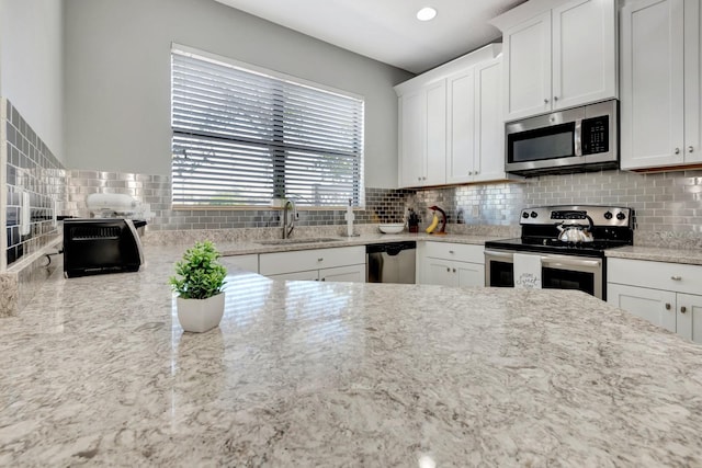 kitchen with light stone countertops, sink, stainless steel appliances, white cabinets, and decorative backsplash