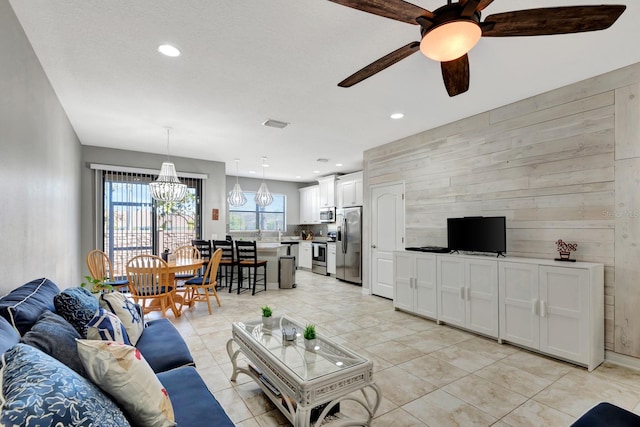 living room with wooden walls and ceiling fan with notable chandelier