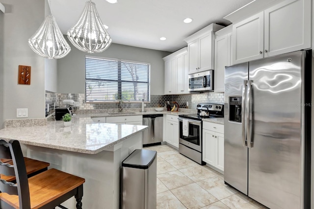 kitchen featuring a breakfast bar area, kitchen peninsula, decorative light fixtures, white cabinetry, and appliances with stainless steel finishes