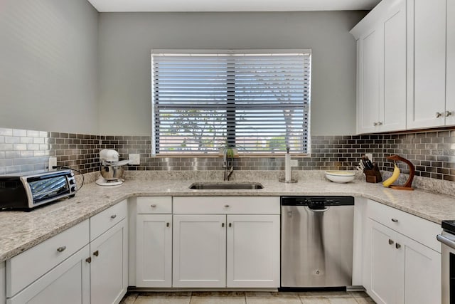 kitchen with sink, stainless steel dishwasher, white cabinets, light stone counters, and tasteful backsplash