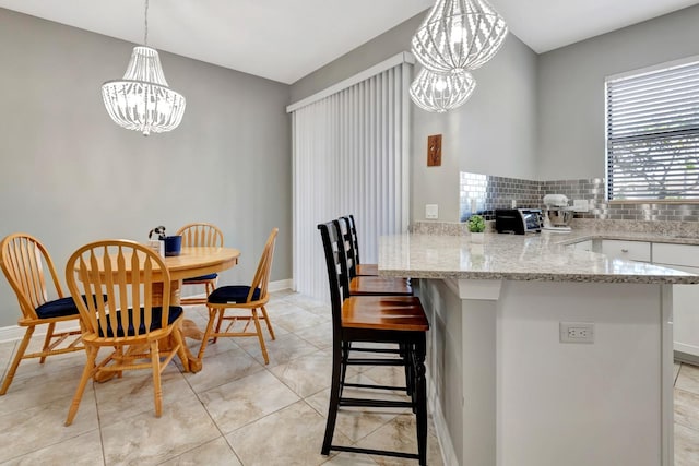 kitchen featuring hanging light fixtures, white cabinets, light stone counters, decorative backsplash, and a chandelier