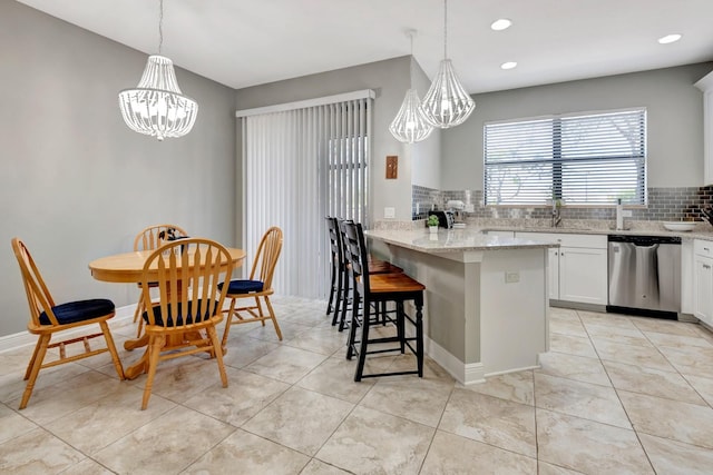 kitchen with decorative backsplash, white cabinets, hanging light fixtures, light stone countertops, and stainless steel dishwasher