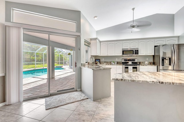 kitchen with ceiling fan, white cabinets, light stone counters, lofted ceiling, and stainless steel appliances