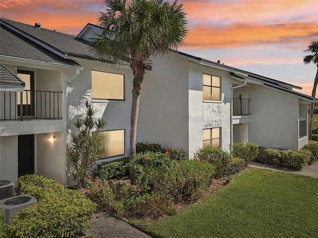 property exterior at dusk featuring central AC, a lawn, and a balcony