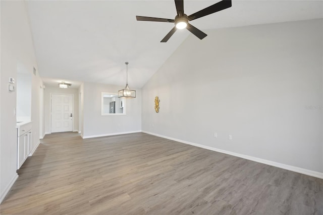 empty room featuring high vaulted ceiling, ceiling fan with notable chandelier, and hardwood / wood-style floors