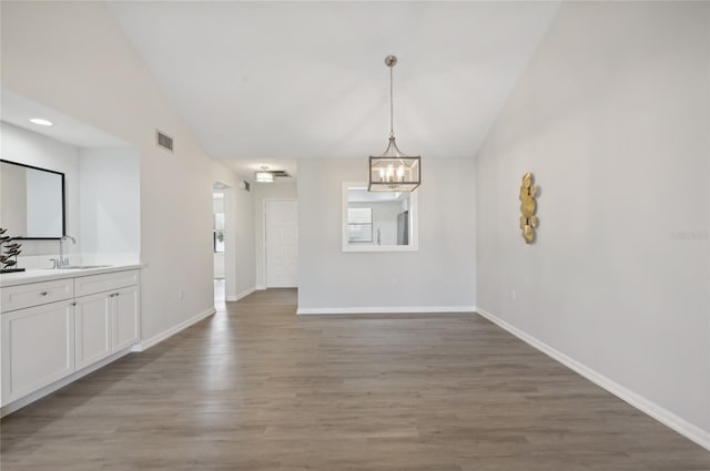 unfurnished dining area featuring sink, vaulted ceiling, wood-type flooring, and an inviting chandelier