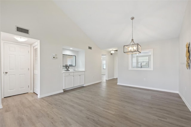 unfurnished living room featuring sink, a chandelier, high vaulted ceiling, and light wood-type flooring