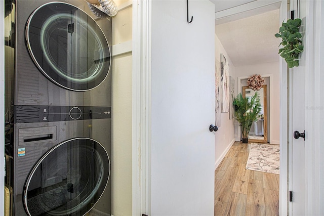 washroom with light wood-type flooring, a textured ceiling, and stacked washer and clothes dryer