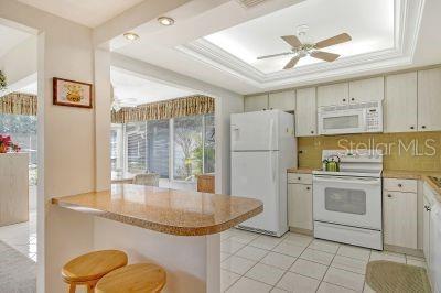 kitchen featuring decorative backsplash, kitchen peninsula, a tray ceiling, a kitchen bar, and white appliances