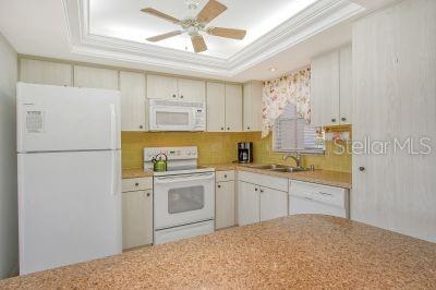 kitchen featuring white appliances, ceiling fan, a raised ceiling, and sink