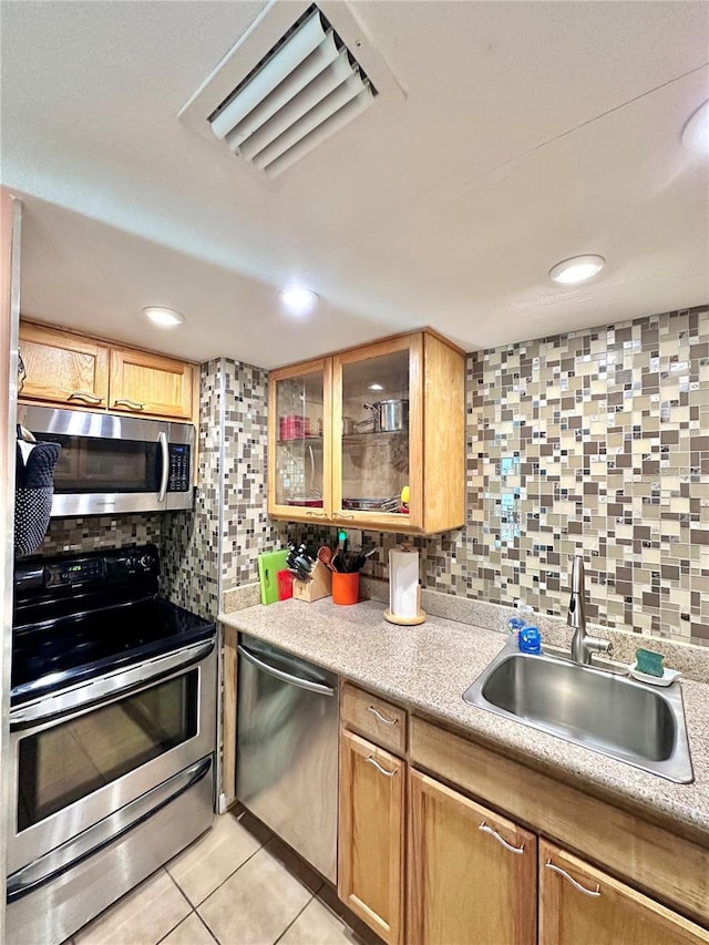 kitchen featuring backsplash, light countertops, a sink, light tile patterned flooring, and appliances with stainless steel finishes