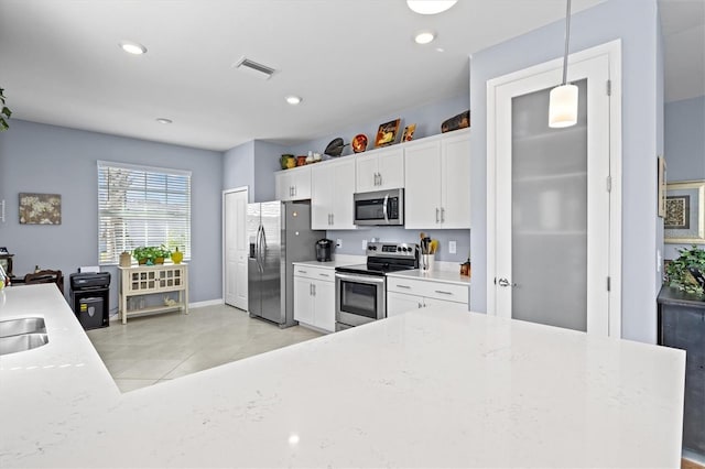 kitchen featuring appliances with stainless steel finishes, hanging light fixtures, white cabinetry, light stone counters, and light tile patterned floors