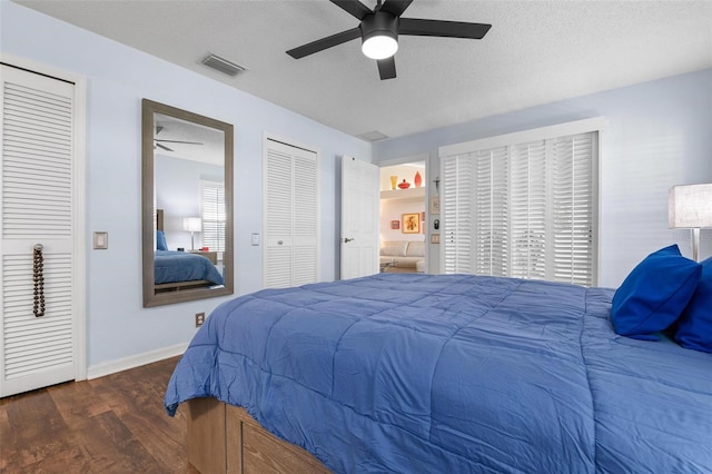 bedroom with ceiling fan, two closets, a textured ceiling, and dark hardwood / wood-style flooring