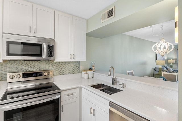 kitchen featuring sink, white cabinetry, stainless steel appliances, decorative backsplash, and an inviting chandelier