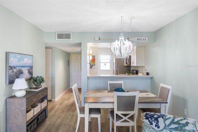 dining area featuring an inviting chandelier, a textured ceiling, and light wood-type flooring