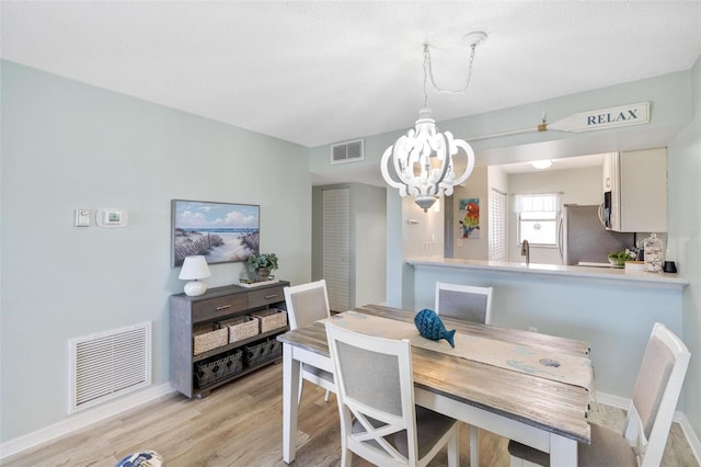 dining area with sink, a chandelier, and light wood-type flooring