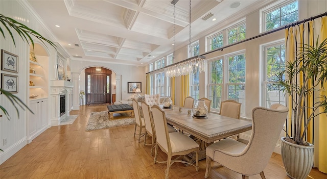 dining room with coffered ceiling, built in features, beamed ceiling, crown molding, and light wood-type flooring