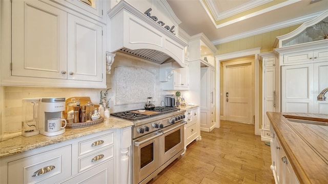 kitchen with white cabinets, light hardwood / wood-style floors, range with two ovens, and wooden counters