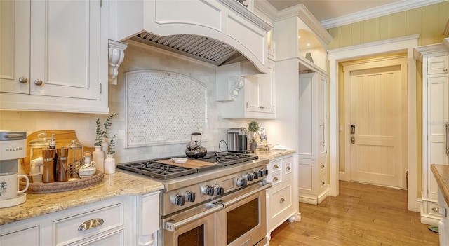 kitchen with light stone countertops, custom exhaust hood, range with two ovens, and white cabinetry