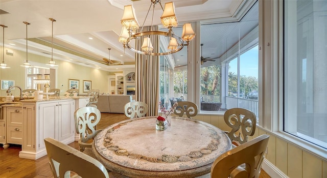 dining space featuring ceiling fan with notable chandelier, light hardwood / wood-style floors, a raised ceiling, and crown molding