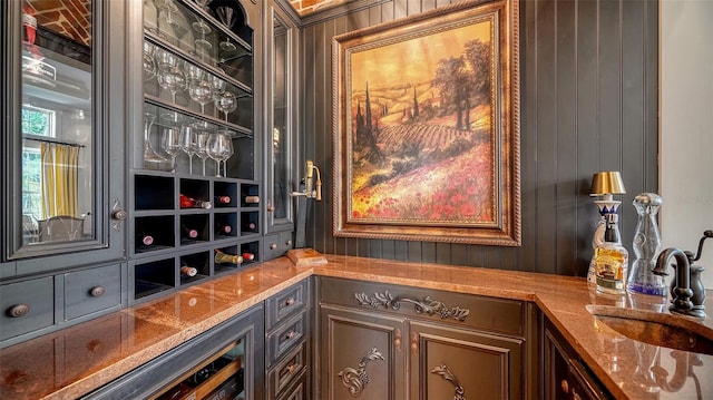 bar featuring sink, stone countertops, dark brown cabinetry, and wood walls