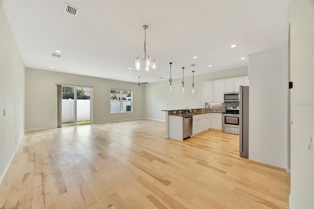 kitchen with decorative backsplash, hanging light fixtures, white cabinets, light wood-type flooring, and appliances with stainless steel finishes