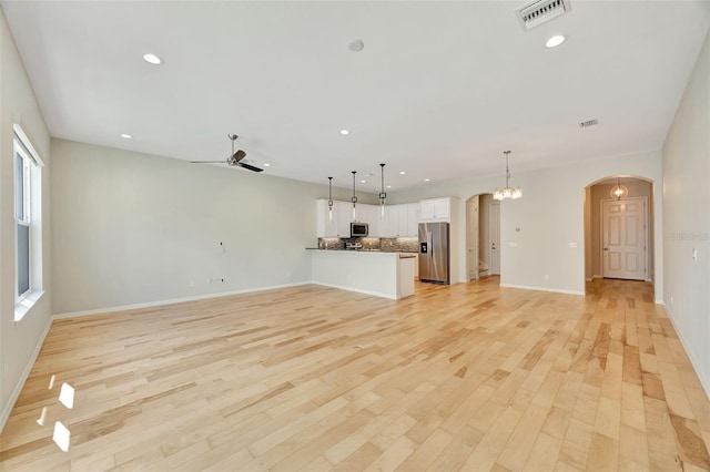 unfurnished living room featuring ceiling fan with notable chandelier and light hardwood / wood-style floors