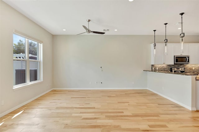 kitchen featuring light hardwood / wood-style flooring, hanging light fixtures, stainless steel appliances, dark stone countertops, and white cabinets