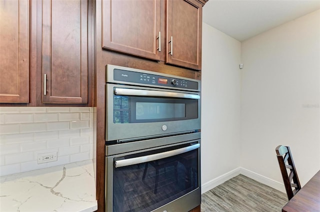 kitchen featuring light hardwood / wood-style floors, light stone countertops, backsplash, and stainless steel double oven