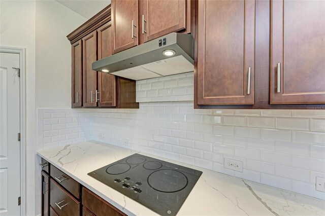 kitchen with black electric stovetop, light stone countertops, and decorative backsplash