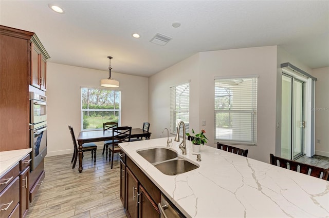 kitchen featuring light stone counters, sink, hanging light fixtures, and light wood-type flooring