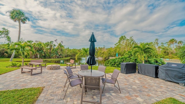 view of patio with area for grilling, a water view, and a fire pit