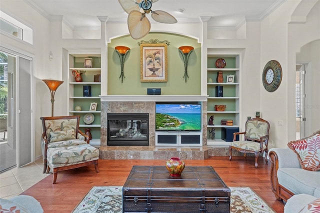 living room featuring built in shelves, crown molding, hardwood / wood-style floors, and a tile fireplace