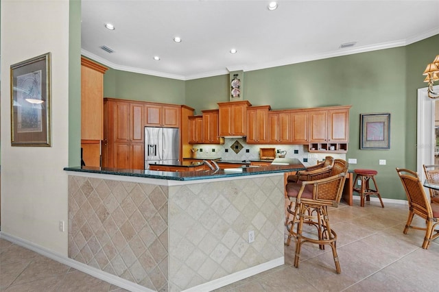 kitchen featuring stainless steel fridge, light tile patterned floors, ornamental molding, kitchen peninsula, and a breakfast bar area