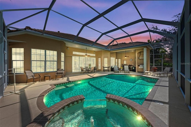 pool at dusk featuring ceiling fan, a patio area, an in ground hot tub, and glass enclosure