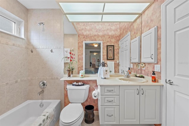 full bathroom featuring tile walls, vanity, tiled shower / bath combo, and toilet