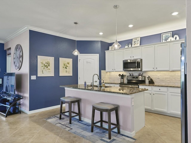 kitchen featuring appliances with stainless steel finishes, white cabinets, dark stone countertops, and an island with sink