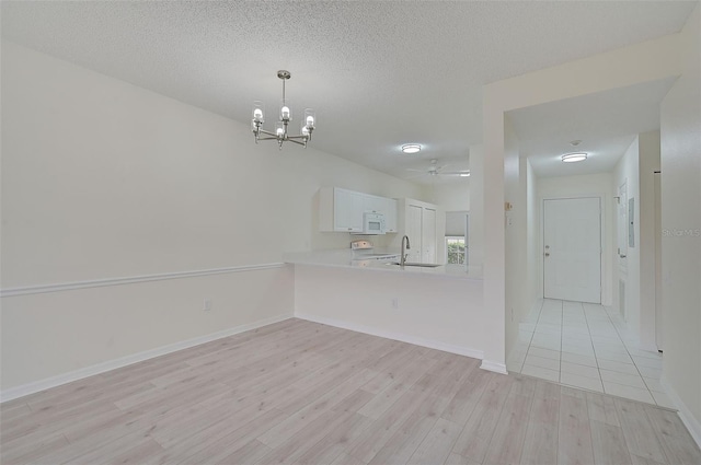 unfurnished dining area featuring sink, light hardwood / wood-style flooring, a textured ceiling, and ceiling fan with notable chandelier