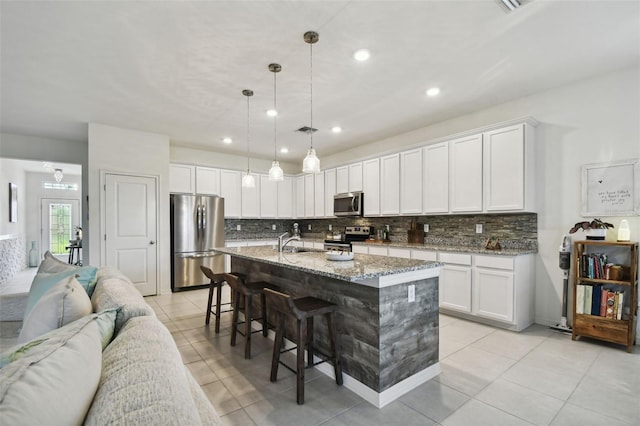 kitchen with white cabinets, a kitchen island with sink, stainless steel appliances, and hanging light fixtures