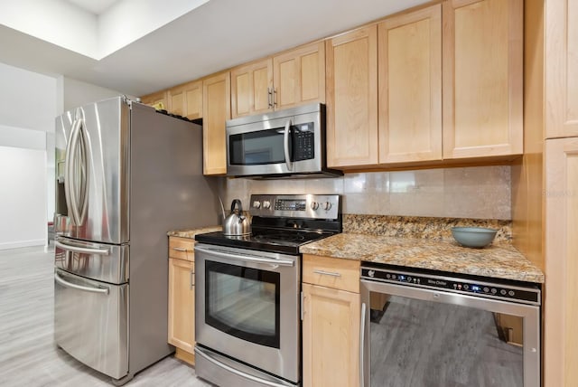 kitchen with light brown cabinets, tasteful backsplash, light stone counters, light wood-type flooring, and stainless steel appliances