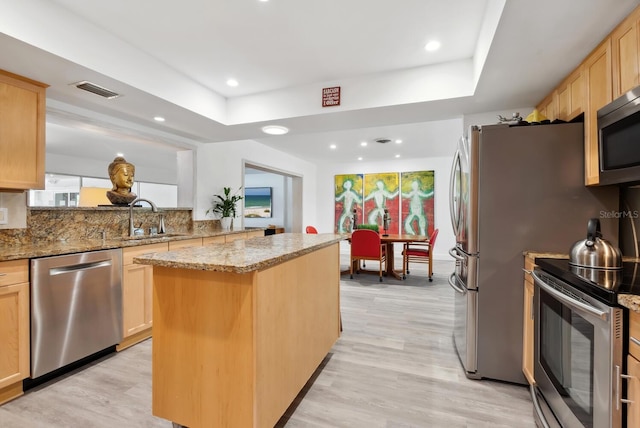 kitchen featuring stainless steel appliances, sink, light brown cabinetry, and a kitchen island