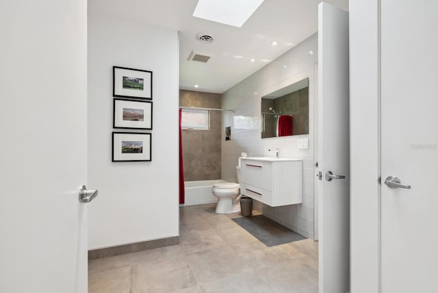 full bathroom with a skylight, toilet, tile patterned floors, tiled shower / bath, and vanity