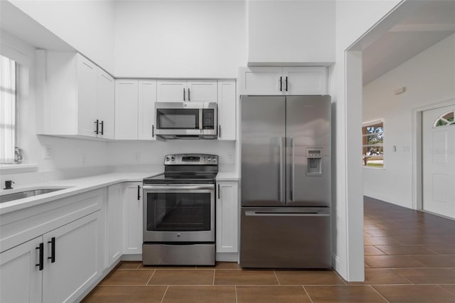 kitchen featuring white cabinetry, appliances with stainless steel finishes, a towering ceiling, and sink