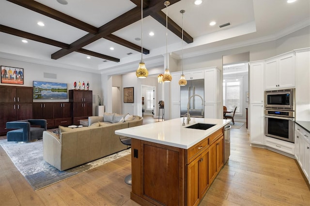 kitchen with white cabinets, a center island with sink, sink, light hardwood / wood-style flooring, and built in appliances