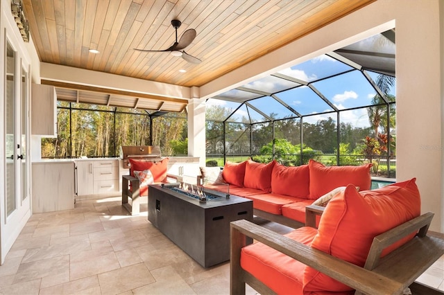 view of patio with glass enclosure, ceiling fan, an outdoor living space with a fire pit, and an outdoor kitchen