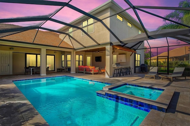 pool at dusk featuring glass enclosure, an outdoor living space, exterior bar, ceiling fan, and a patio